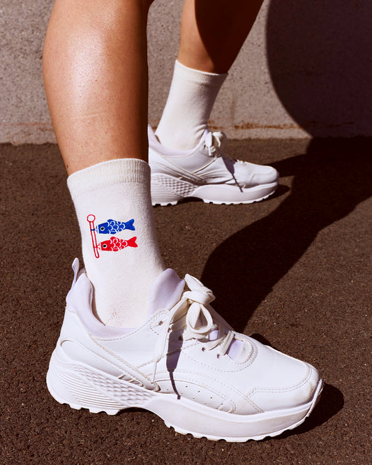 White athletic socks with a red and blue fish Koinobori Carp flag graphic, worn with chunky white sneakers on a dark asphalt surface.